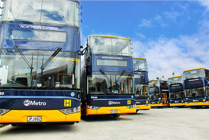Double-decker AT metro buses parked in a row under a clear blue sky.