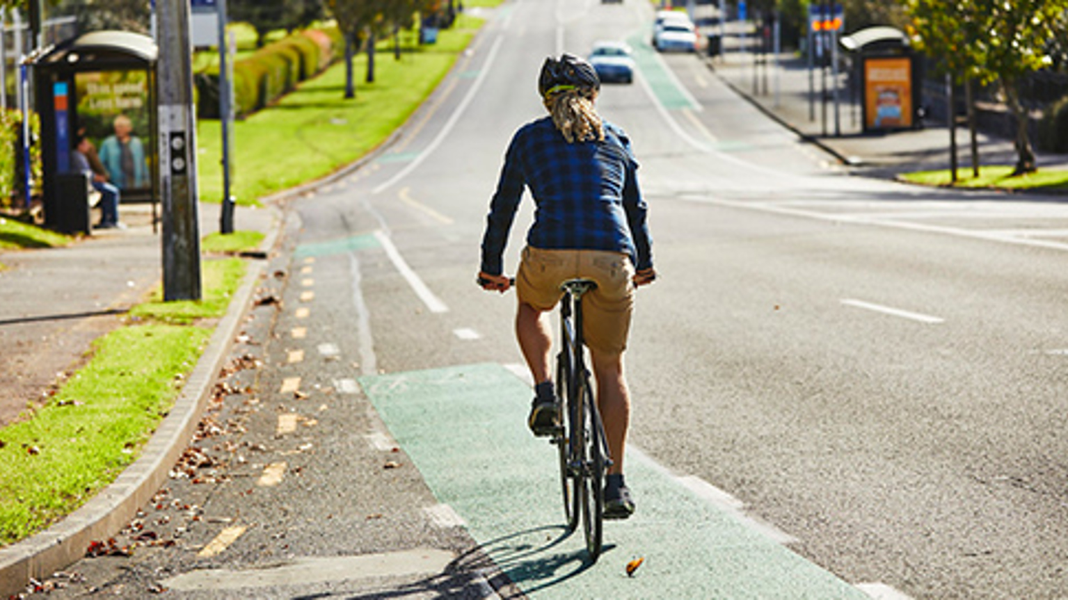 A cyclist rides a bike on a on-road cycle lane near the road kerb. There are no cars on the road.