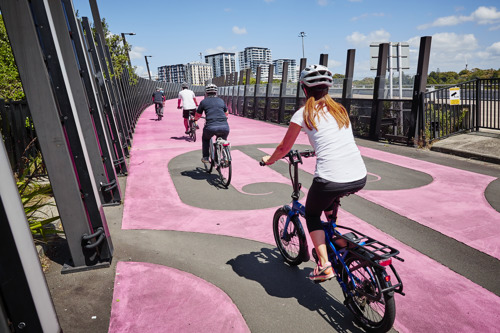Four cyclists ride bikes along the pink light path.