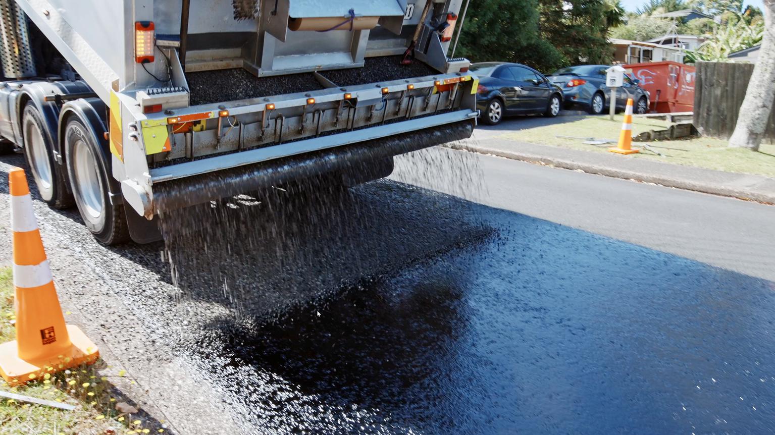 Truck pouring chipseal onto a road.