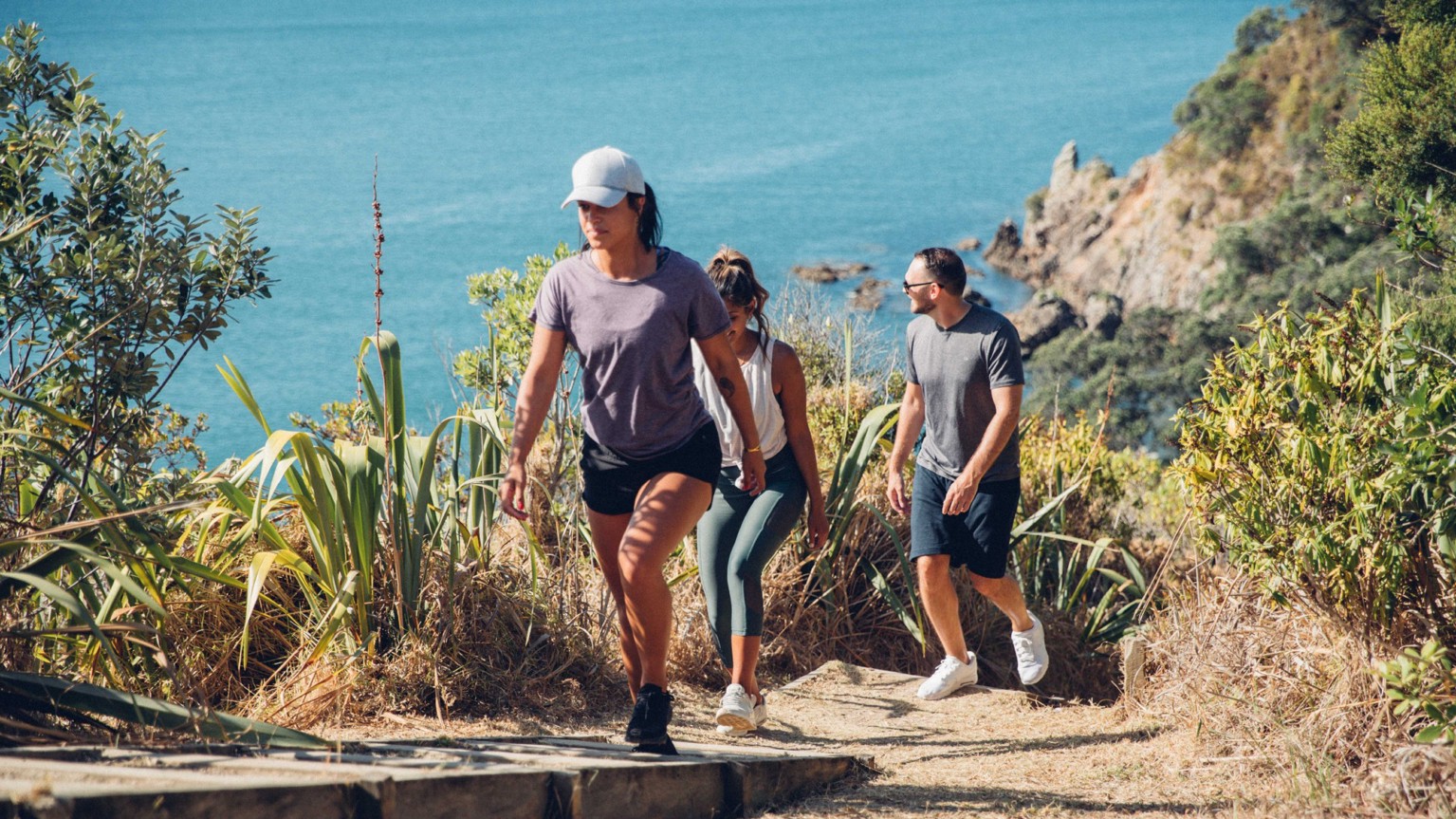Woman walking uphill amongst trees with the sea in the background.