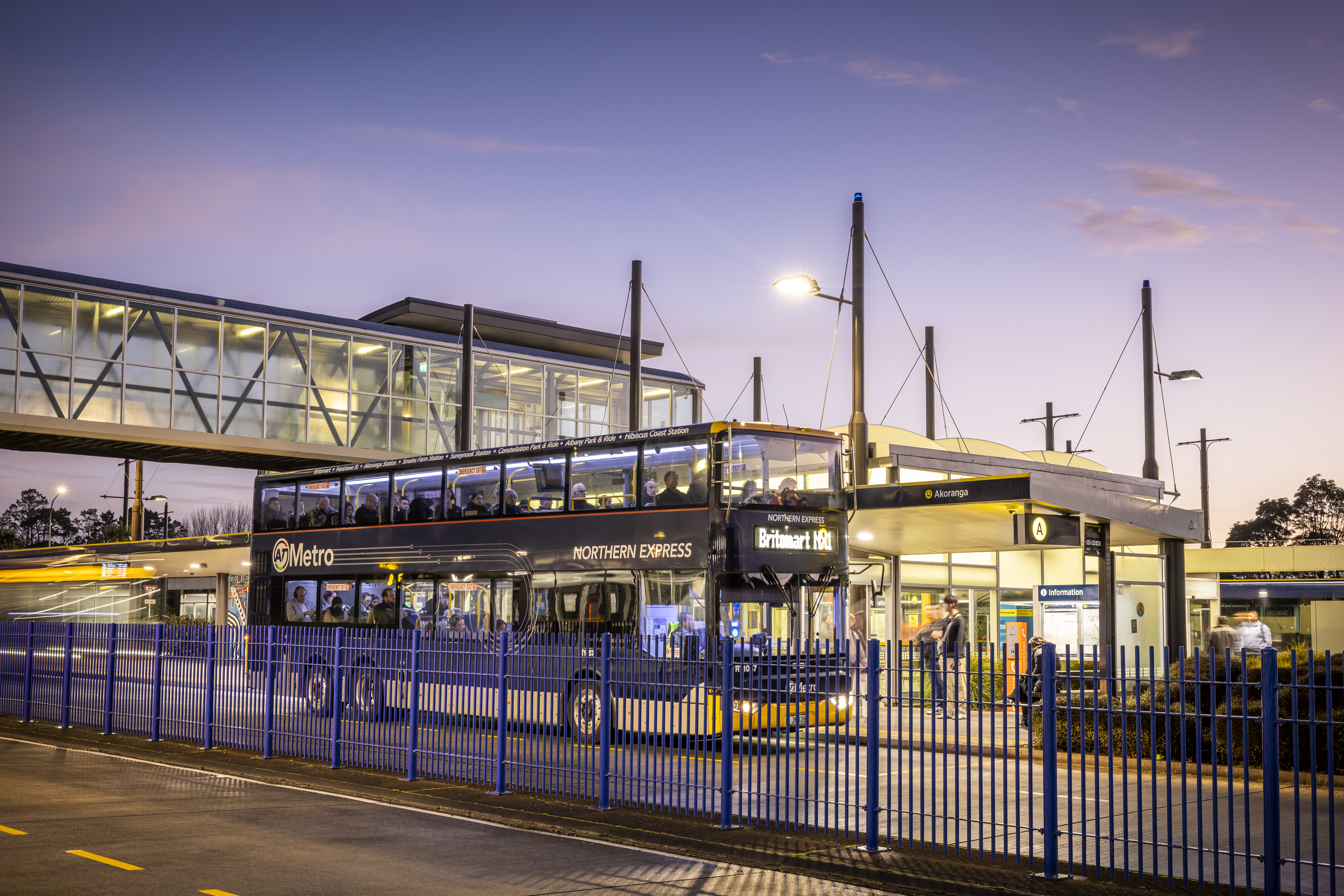 A bus stop with a double-decker bus parked in front of it at nighttime.