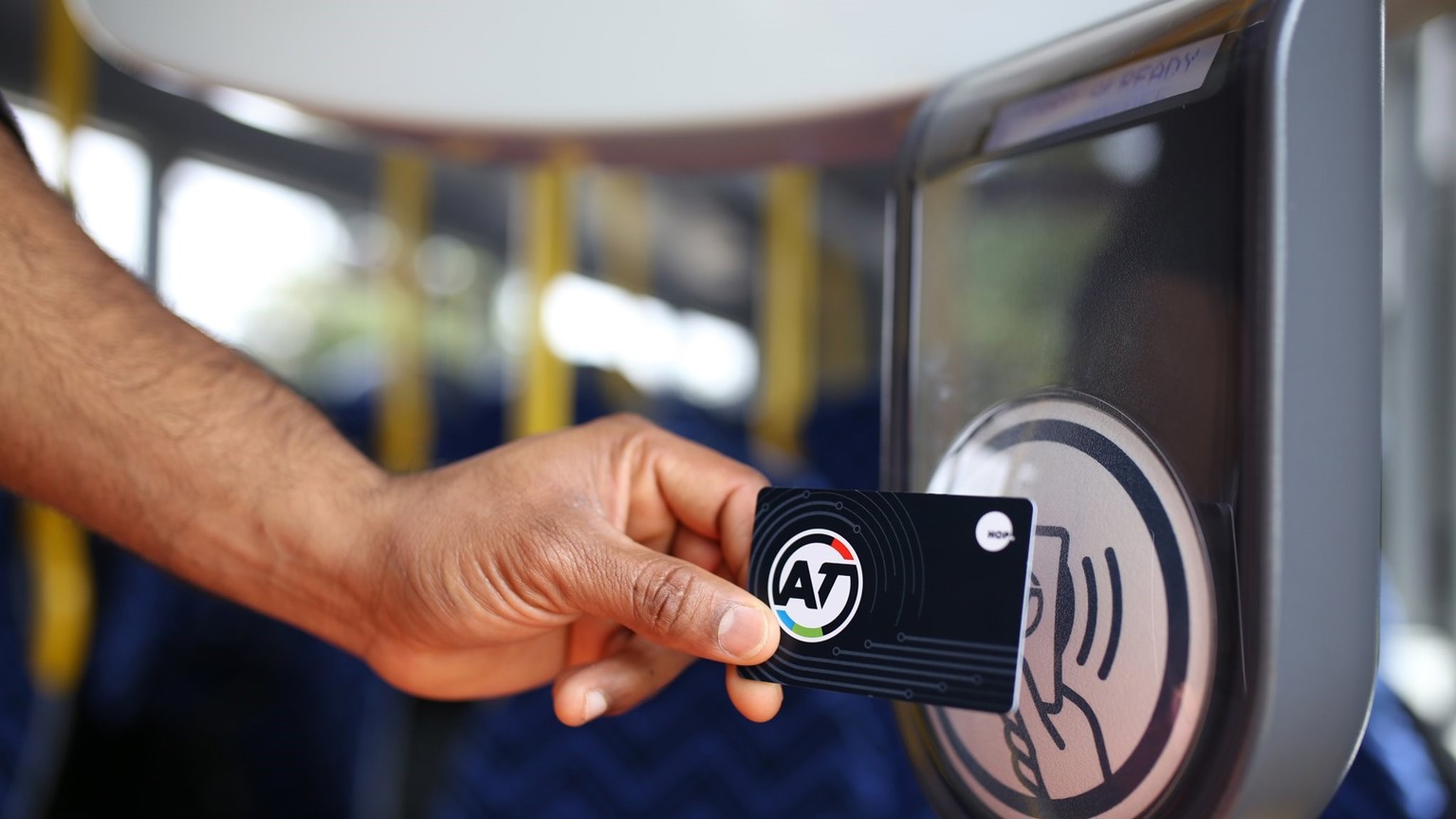A public transport user is on a bus shown to hold their AT Hop card against the onboard card reader to tag off or on.