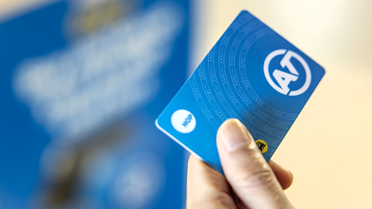 A person's hand holding an AT HOP card against the card reader on a bus
