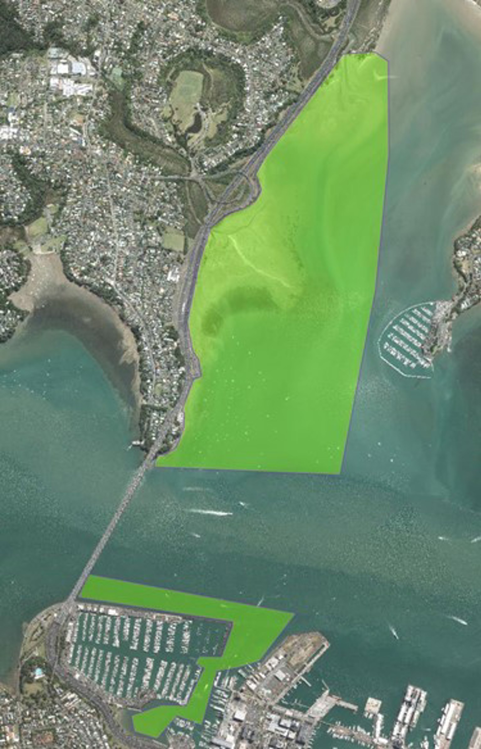Aerial view of coastal area with two large green shaded zones near a bridge and marina.