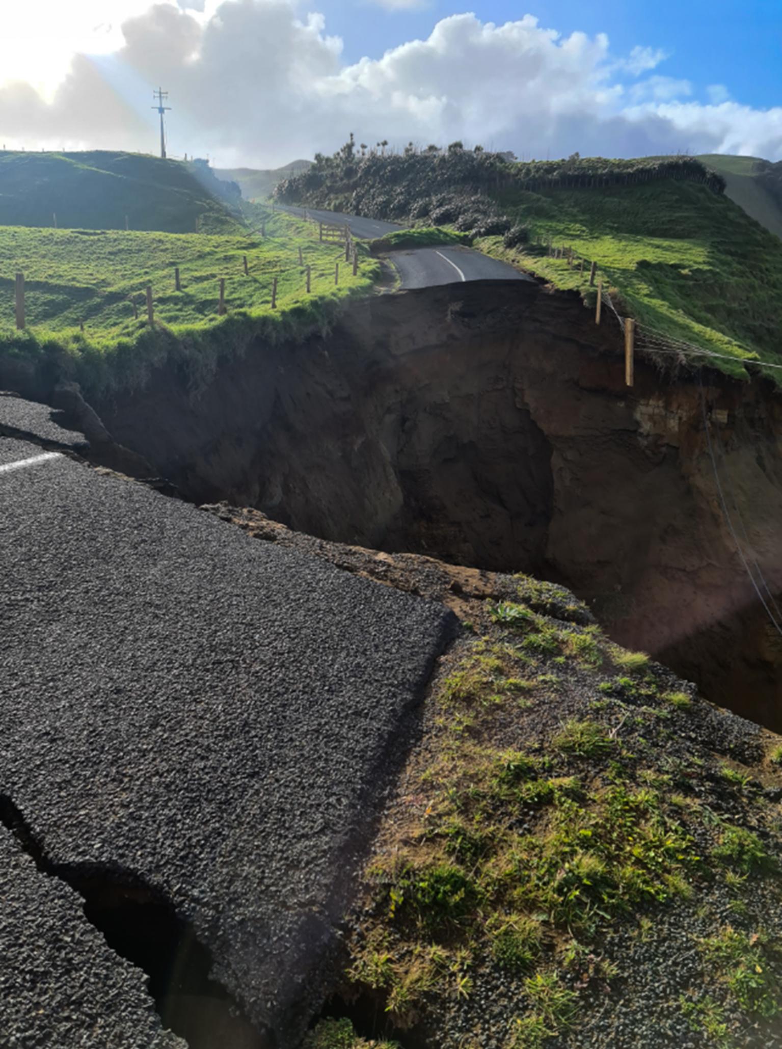 A rural road with a large chunk missing from it due to a landslide.