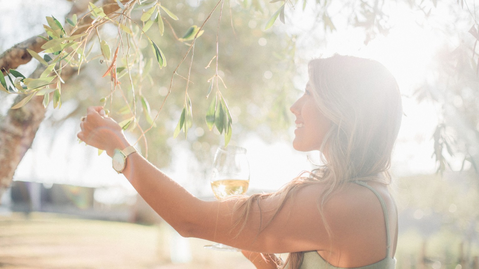 Woman touching tree holding wine glass.